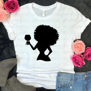 May include: A white t-shirt with a black silhouette of a woman with an afro holding a glass of wine.