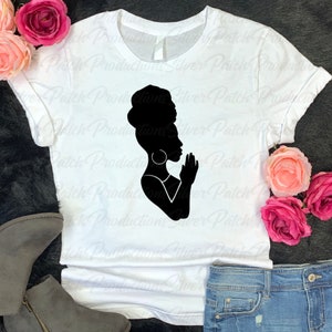 May include: A white t-shirt with a black silhouette of a woman with her hands clasped in prayer. The woman is wearing a headscarf and large earrings.