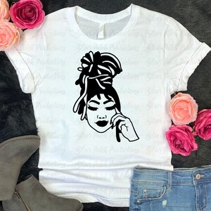 May include: A white t-shirt with a black silhouette of a woman with dreadlocks styled in a bun. The woman is wearing a relaxed expression and has her eyes closed.