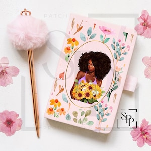 May include: A pink notebook with a floral design and a woman with brown hair holding a bouquet of sunflowers. The notebook has a gold elastic band closure and the text "PATCH" is printed on the cover.