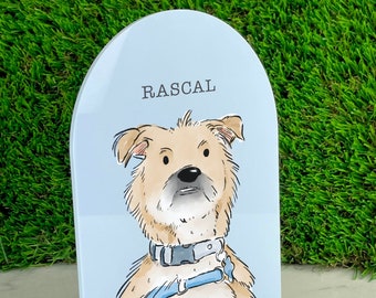 Puede incluir: Un soporte de acrílico azul claro con una parte superior redondeada presenta una ilustración de dibujos animados de un perro marrón y blanco con un collar azul y una correa. El nombre del perro, "RASCAL", está impreso en negro en la parte superior del soporte.