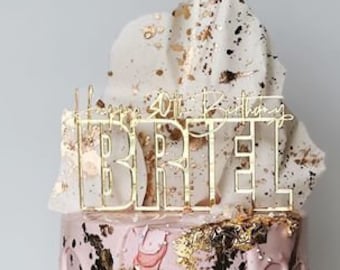 May include: A pink cake with gold leaf and white frosting. The cake is decorated with a gold topper that says "Happy 30th Birthday Briel".