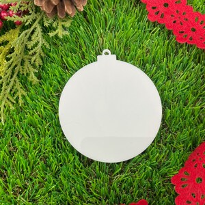 May include: White blank round ornament with a loop at the top, sitting on a green artificial grass surface.