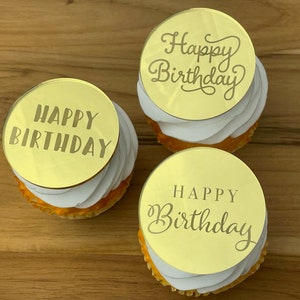 Może przedstawiać: Trzy złote ozdoby do babeczek z napisem "Happy Birthday" w r&oacute;żnych czcionkach. Ozdoby znajdują się na białych babeczkach.