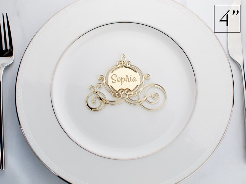 Op de afbeelding: Gouden Assepoester-koets-kaartjeshouder met de naam "Sophia" op een wit bord. De kaartjeshouder heeft een diameter van 10 cm.