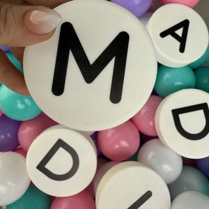May include: White plastic circles with black letters spelling out the word "MAD" in a pile of colorful plastic balls.
