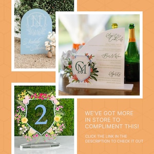 Puede incluir: Tres letreros de boda de acr&iacute;lico con dise&ntilde;os florales. El primer letrero es azul claro con un monograma blanco y el texto "Natalie y Thomas". El segundo letrero es blanco con un dise&ntilde;o floral y un monograma verde "CM". El tercer letrero es una corona de flores con un escudo azul en el centro con el n&uacute;mero "2" en &eacute;l.