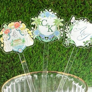 Puede incluir: Tres toppers de pastel de acr&iacute;lico transparente con dise&ntilde;os florales e iniciales personalizadas. Los toppers presentan un gato blanco, una palmera y una mariposa.