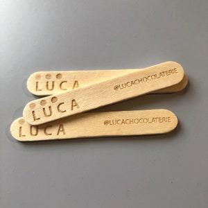 May include: Three wooden popsicle sticks with the word "LUCA" and the text "@LUCACHOCOLATERIE" printed on them.