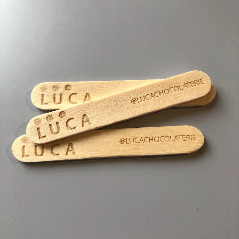 May include: Three wooden popsicle sticks with the word "LUCA" and the text "@LUCACHOCOLATERIE" printed on them.