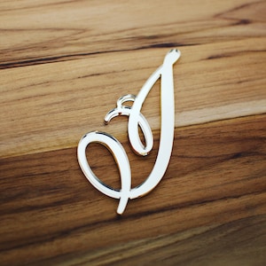 May include: A silver mirrored letter I in a cursive font. The letter is on a wooden surface.