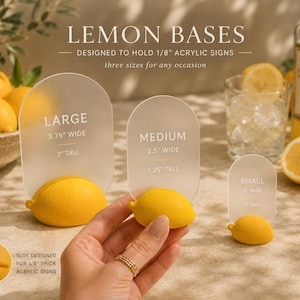 May include: Three yellow lemon-shaped bases designed to hold 1/8 inch thick acrylic signs. The bases come in large, medium, and small sizes, with clear acrylic inserts labeled with their respective dimensions in inches. A slot is visible on the base.