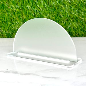 May include: A white acrylic display stand with a semi-circular frosted panel. The stand has a flat base and a raised platform.