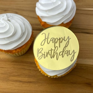 Może przedstawiać: Złoty topper do babeczek z napisem "Happy Birthday" na białej babeczce z białym lukrem.