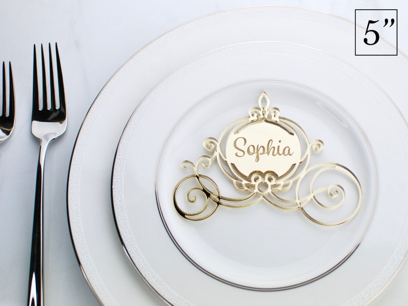 Op de afbeelding: Gouden glitter Assepoester koets plaatskaart houder met de naam "Sophia" erop geschreven. De plaatskaart is 5 inch hoog.