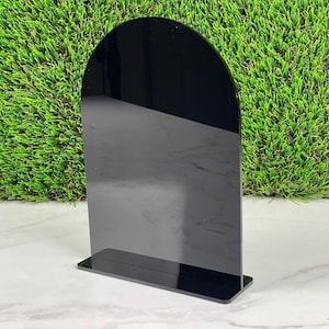 May include: Black acrylic display stand with a rounded top. The stand is designed to hold a sign or other display item.