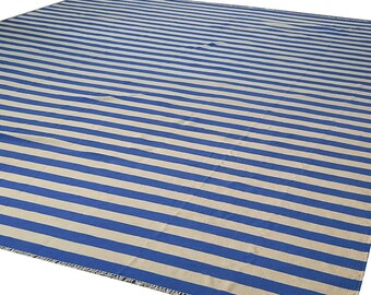 May include: A large rectangular rug with horizontal stripes in alternating shades of blue and beige. The rug has a fringed edge and is suitable for indoor or outdoor use.