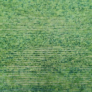 Puede incluir: Primer plano de una alfombra verde con un patr&oacute;n horizontal texturizado. La alfombra tiene un pelo denso y rizado, creando una apariencia suave y afelpada. El color es un verde vibrante y natural, lo que sugiere un producto hecho a mano o de fibra natural.