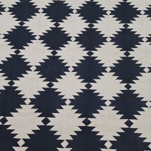Puede incluir: Una alfombra tejida con un patr&oacute;n geom&eacute;trico repetitivo. El dise&ntilde;o presenta formas de diamante alternas en azul marino y blanco roto. La textura de la alfombra parece suave y adecuada para uso en interiores.