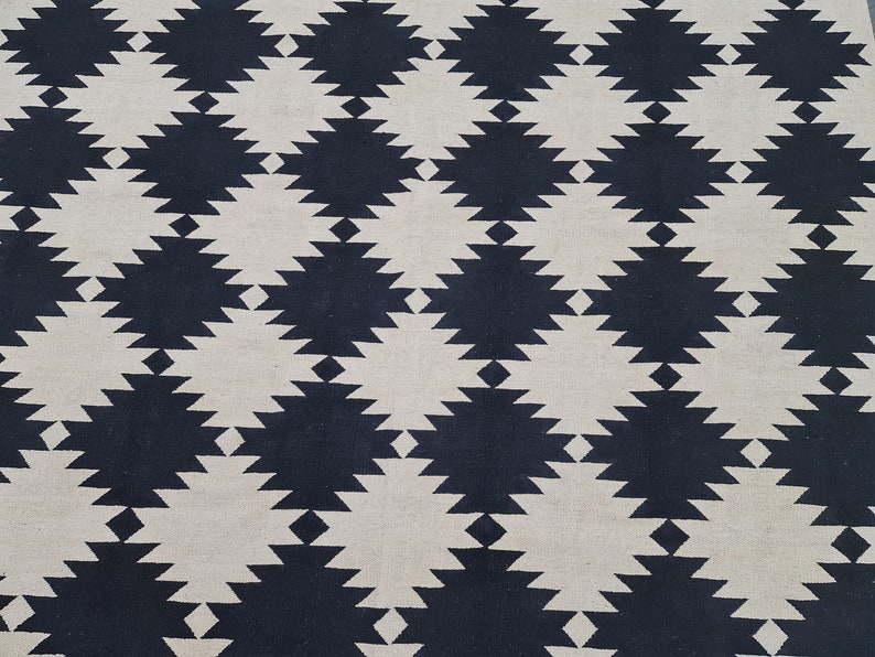 Puede incluir: Una alfombra tejida con un patr&oacute;n geom&eacute;trico repetitivo. El dise&ntilde;o presenta formas de diamante alternas en azul marino y blanco roto. La textura de la alfombra parece suave y adecuada para uso en interiores.