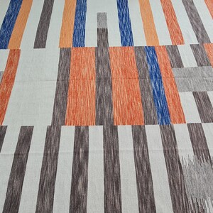 May include: Geometric patterned fabric featuring vertical stripes in shades of orange, blue, brown, and gray against a white background. The design has a modern, abstract aesthetic, suitable for home decor or textile projects.