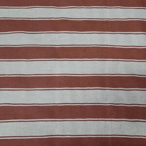 May include: A textile with a repeating pattern of horizontal stripes. The stripes alternate between a muted reddish-brown and a light beige color. The fabric appears to be woven, with a slightly textured surface.
