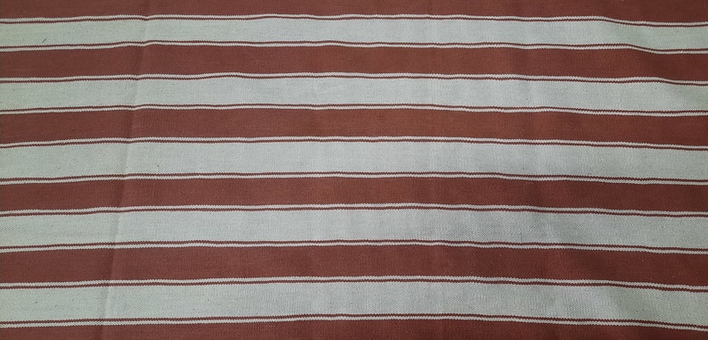 May include: A textile with a repeating pattern of horizontal stripes. The stripes alternate between a muted reddish-brown and a light beige color. The fabric appears to be woven, with a slightly textured surface.