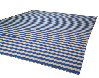 May include: A large rectangular rug with horizontal stripes in alternating shades of blue and beige. The rug has a fringed edge on one side. The stripes are evenly spaced across the surface of the rug.