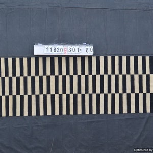May include: A rectangular rug with a repeating pattern of vertical black stripes alternating with beige stripes. The rug is approximately 30 inches long and 80 inches wide. The rug is made of a woven material.