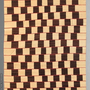 May include: A rectangular woven rug with a repeating pattern of alternating dark brown and beige blocks. Thin red lines separate the rows of blocks, creating a visually dynamic design. The rug's texture suggests a handmade quality.