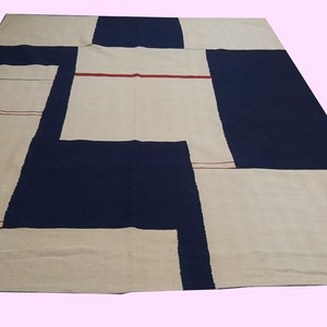 Op de afbeelding: Een groot, rechthoekig tapijt met een geometrisch ontwerp. Het tapijt heeft een patchworkpatroon van marineblauwe, gebroken witte en beige secties. Dunne rode lijnen accentueren enkele van de gebroken witte panelen. Geschikt voor een woon- of slaapkamer.