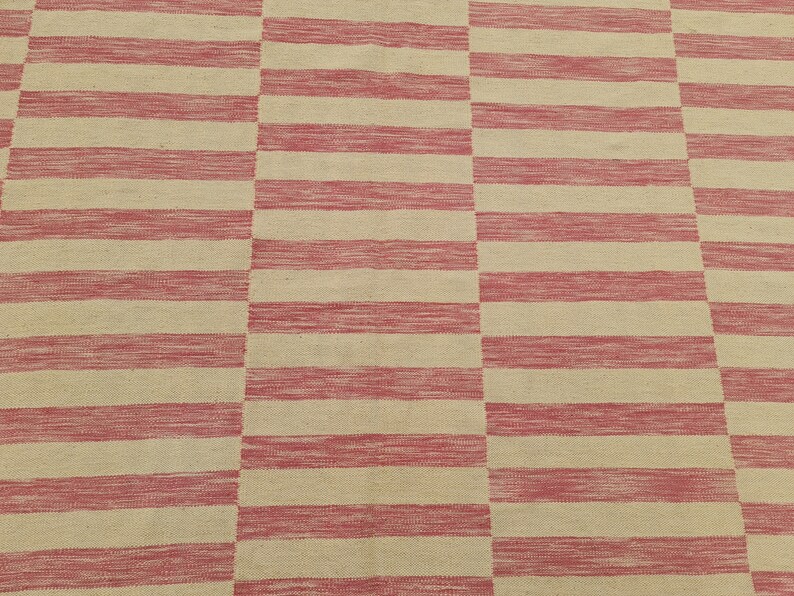 May include: A rectangular rug with a repeating pattern of alternating red and beige horizontal stripes. The stripes are thick and evenly spaced, creating a bold, geometric design. The rug appears to be made of woven fabric.