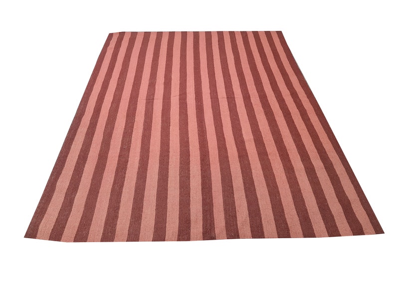 May include: A rectangular rug with vertical stripes in shades of pink and brown. The rug's design features alternating wide stripes, creating a bold and visually appealing pattern. The rug is likely made of woven material.
