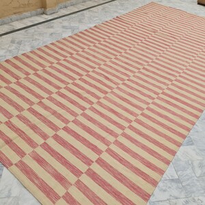 May include: A large rectangular rug with a repeating pattern of alternating red and beige stripes. The stripes run horizontally and vertically, creating a checkered design. The rug is made of a woven material.