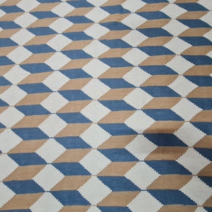 May include: Geometric patterned rug featuring a repeating 3D cube design. The rug's pattern uses a combination of white, blue, and tan colors. The design creates an optical illusion of depth and dimension, suitable for home decor.