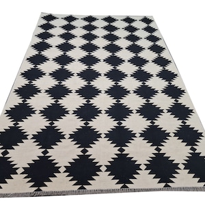 Puede incluir: Una alfombra rectangular con un patr&oacute;n repetido de formas de diamante negras sobre un fondo crema. La alfombra tiene un dise&ntilde;o geom&eacute;trico simple, adecuado para varios estilos de interior. La alfombra est&aacute; hecha de un material tejido.