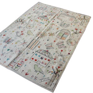 以下が含まれることがあります： クリーム色のテキスタイルに、気まぐれなデザインが刺繍されています。蝶、家、鳥、花、幾何学模様が様々な色で描かれています。縁はコントラストの効いたステッチで仕上げられています。