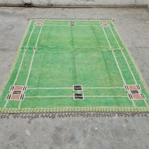May include: A rectangular green rug with a geometric design. The rug features a light green field with white and black rectangular accents. The edges are trimmed with a fringe. The rug's dimensions are approximately 6 x 9 feet.