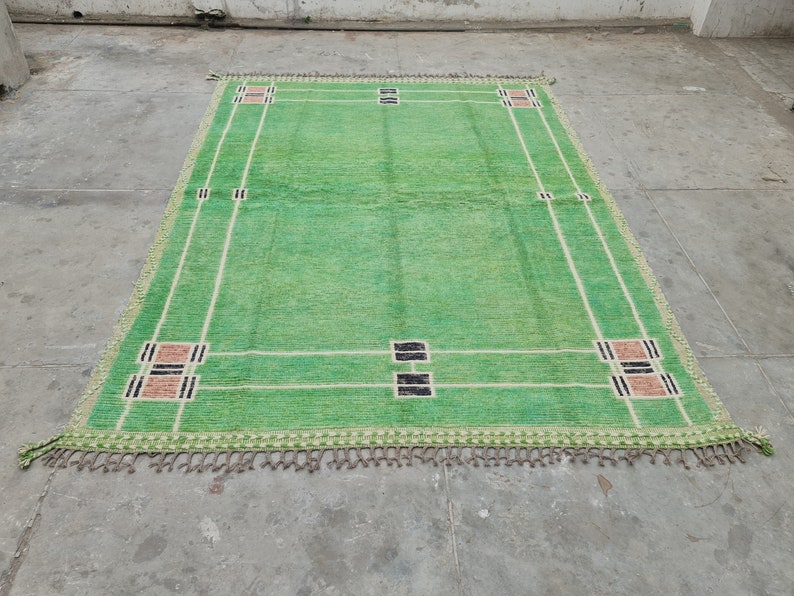 May include: A rectangular green rug with a geometric design. The rug features a light green field with white and black rectangular accents. The edges are trimmed with a fringe. The rug's dimensions are approximately 6 x 9 feet.