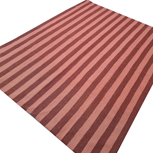 May include: A large, rectangular rug with a striped pattern. Alternating bands of light and dark red-brown run the length of the rug. The rug is made of a woven material and is suitable for use in a living room or bedroom.