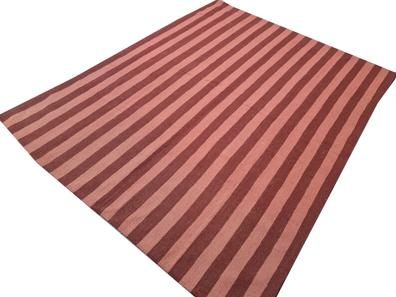 May include: A large, rectangular rug with a striped pattern. Alternating bands of light and dark red-brown run the length of the rug. The rug is made of a woven material and is suitable for use in a living room or bedroom.