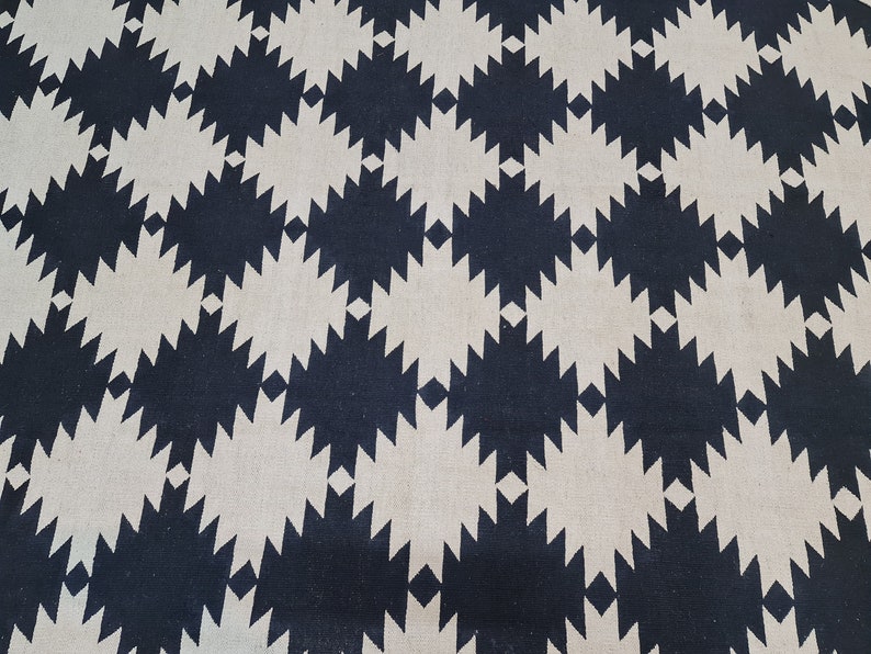 Puede incluir: Primer plano de un textil con un patr&oacute;n geom&eacute;trico repetitivo. El dise&ntilde;o presenta formas de diamante azul marino oscuro y blanco roto alternadas, creando una apariencia texturizada y sim&eacute;trica. La tela parece estar tejida.