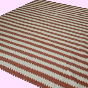 May include: A large, rectangular rug with a repeating pattern of wide, parallel stripes in alternating shades of brown and off-white. The rug is made of a woven material and is suitable for indoor or outdoor use.