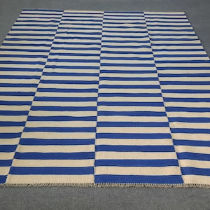 Op de afbeelding: Een rechthoekig tapijt met een blauw-wit streepmotief. Het tapijt heeft afwisselende secties met horizontale strepen, waardoor een dambordeffect ontstaat. Het tapijt meet ongeveer 183 x 244 cm.