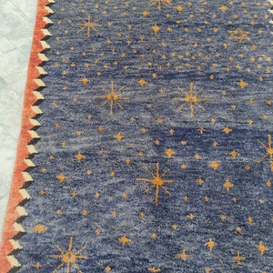 May include: A blue rug with a pattern of yellow starbursts and smaller stars. The rug has a red border with a zigzag design in black and white. The rug is made of a textured material.