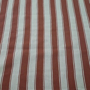 May include: A textile with a repeating pattern of vertical stripes. The stripes alternate between a muted red-brown color and a light beige-white. The fabric appears to be a woven material, possibly cotton or linen.