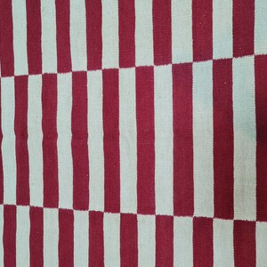 Puede incluir: Textil tejido con un patr&oacute;n repetitivo de rayas verticales rojas y blancas. Las rayas alternan en ancho, creando un dise&ntilde;o visualmente din&aacute;mico. La alfombra o tela tiene una apariencia texturizada.