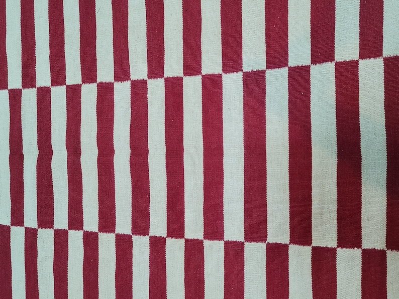 Puede incluir: Textil tejido con un patr&oacute;n repetitivo de rayas verticales rojas y blancas. Las rayas alternan en ancho, creando un dise&ntilde;o visualmente din&aacute;mico. La alfombra o tela tiene una apariencia texturizada.