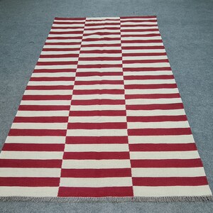 Puede incluir: Alfombra rectangular con rayas horizontales rojas y blancas alternas. La alfombra est&aacute; hecha de material tejido y tiene un patr&oacute;n geom&eacute;trico simple. Adecuada para uso en interiores, mide aproximadamente 200 cm x 140 cm.