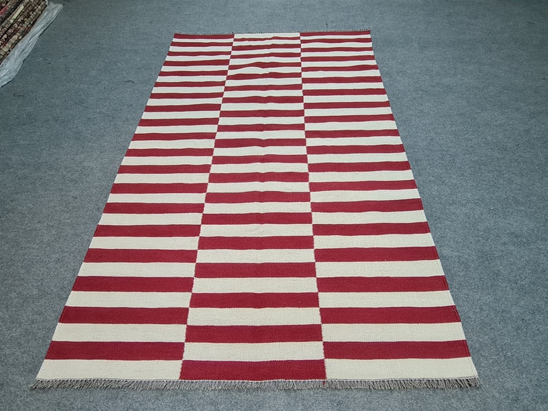Puede incluir: Alfombra rectangular con rayas horizontales rojas y blancas alternas. La alfombra est&aacute; hecha de material tejido y tiene un patr&oacute;n geom&eacute;trico simple. Adecuada para uso en interiores, mide aproximadamente 200 cm x 140 cm.